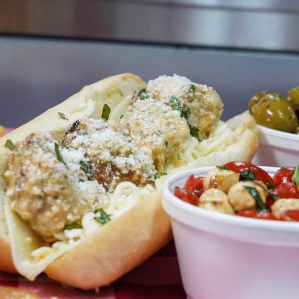 Meatball sub sandwich with parmesan cheese and parsley, with sides of olives and caprese salad.